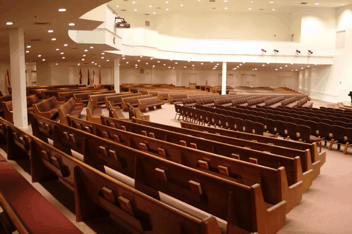 Large church sanctuary full of wooden pews showing long-term aging